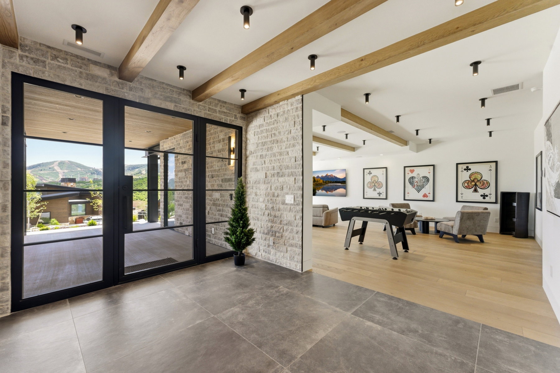 Expansive floor-to-ceiling black-framed glass doors open to an outdoor patio with mountain scenery