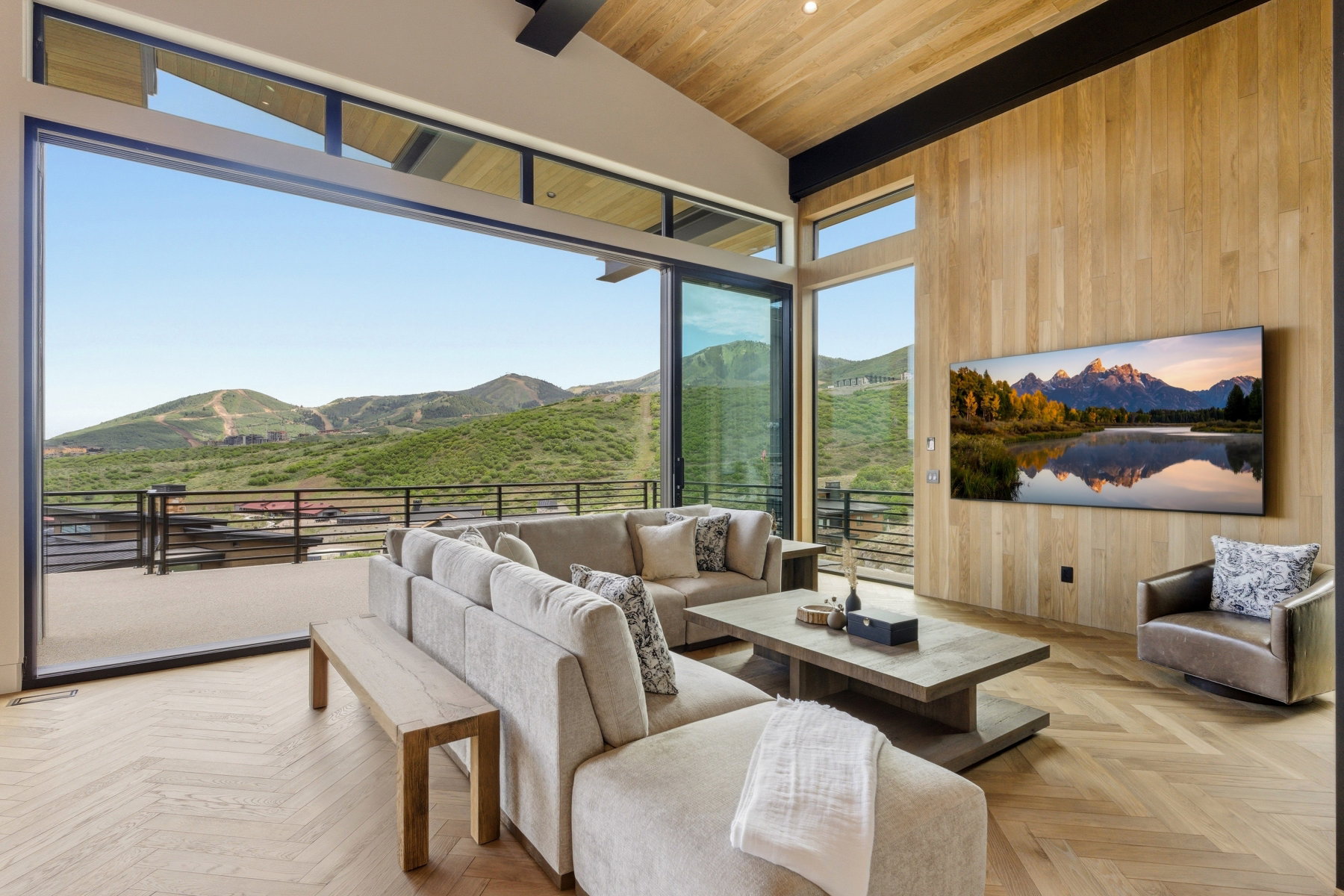 Open-concept living space with expansive sliding glass doors, chevron wood-finish flooring, a vaulted wood-paneled ceiling, a wood-paneled accent wall, and a spacious outdoor balcony with mountain scenery