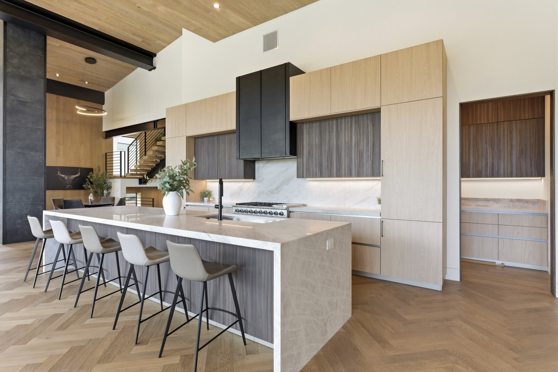 Contemporary kitchen featuring a large island with waterfall countertop, herringbone wood-finish flooring, integrated appliances, two-tone cabinetry, and a full-height marble backsplash
