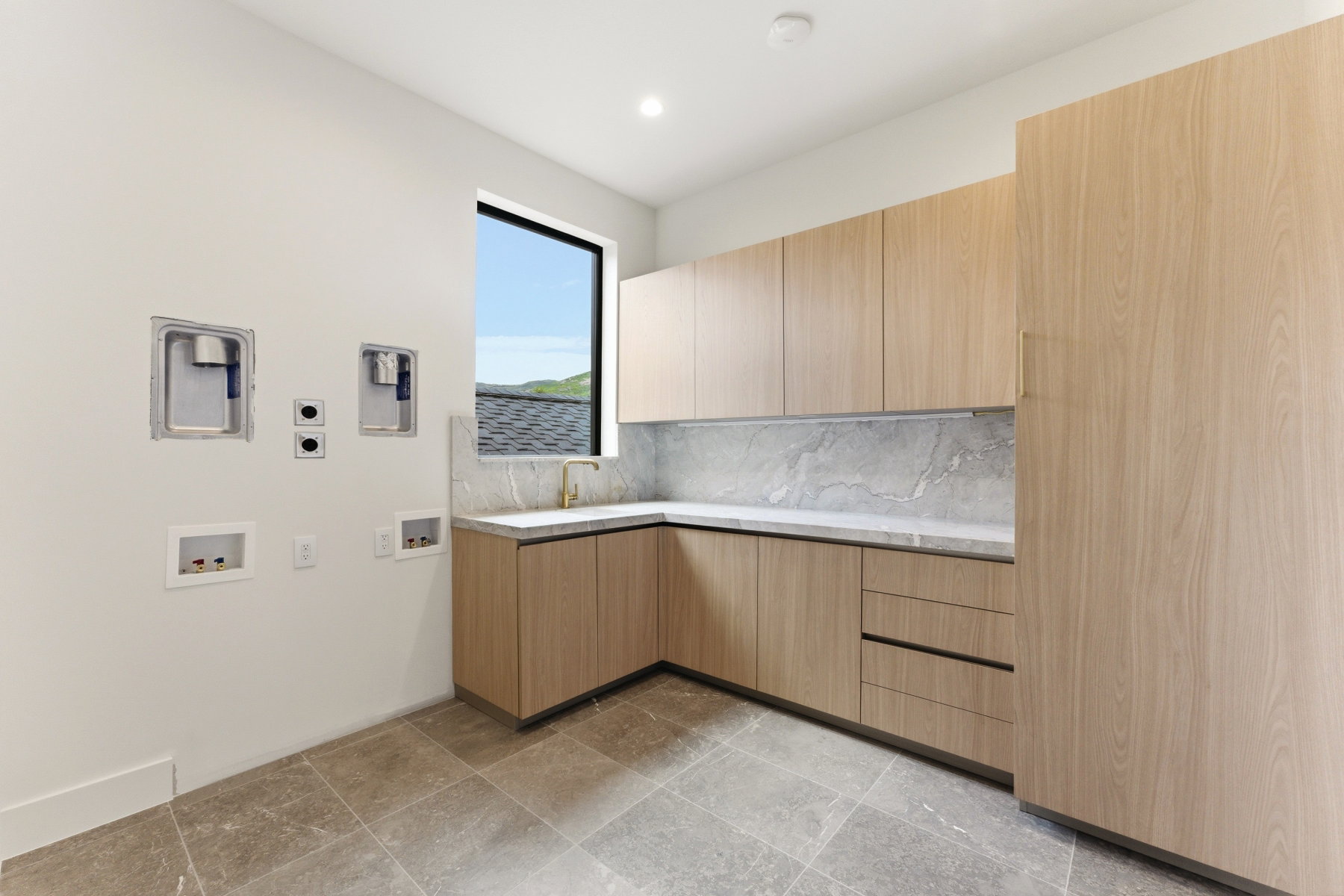 Dedicated laundry area featuring modern cabinetry, a built-in sink with a gooseneck faucet, light-toned stone countertops, and a coordinating stone backsplash