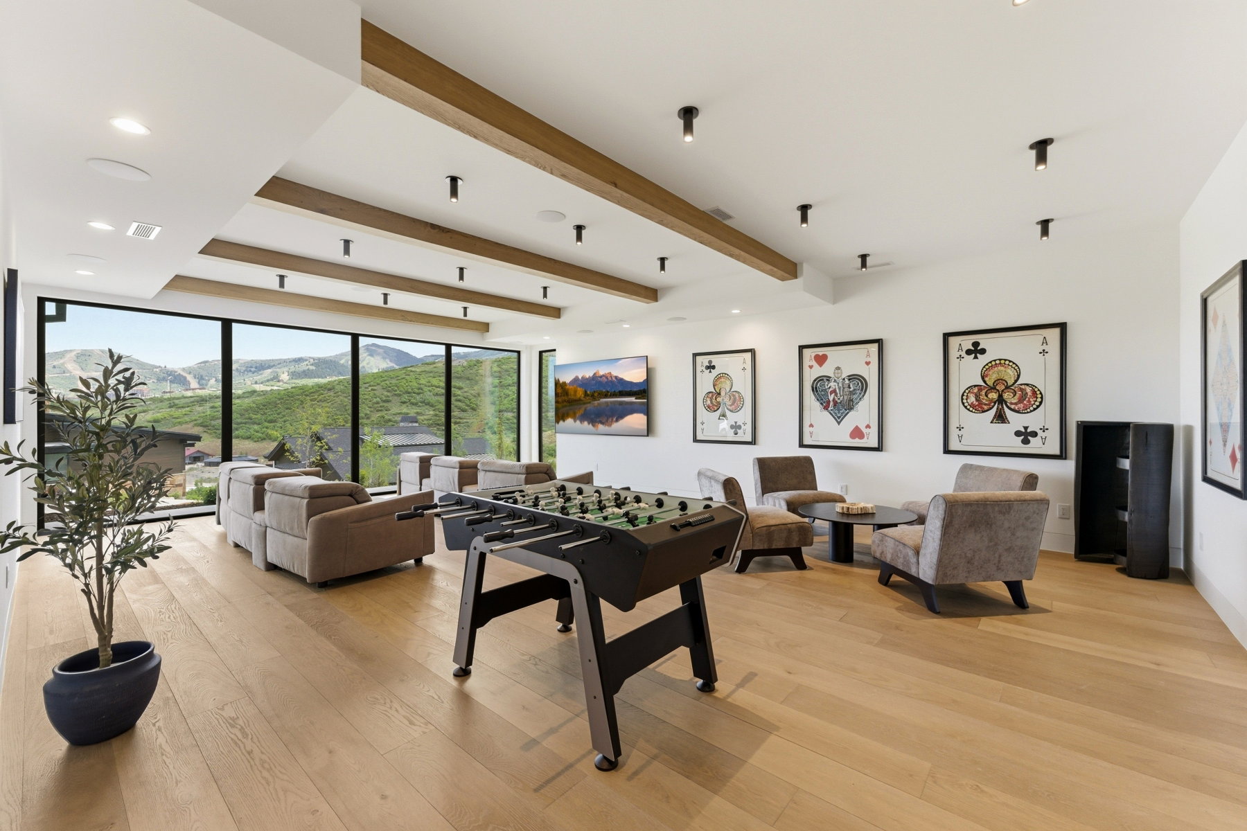 Open-concept living area with expansive floor-to-ceiling windows, light wood-finish flooring, and exposed ceiling beams