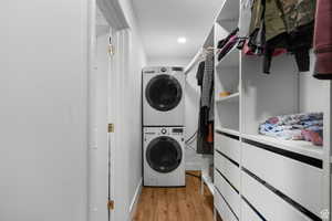 Laundry room inside of walk in closet with light wood finished floors and stacked washer and dryer