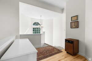 Corridor featuring light wood finished floors, suspended lighting, and an upstairs landing