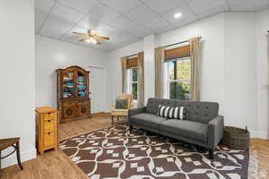 Living room with a paneled ceiling, light wood-style flooring, and ceiling fan