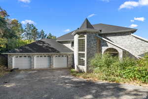 View of front of property exterior featuring an attached garage, a shingled roof, driveway, and brick siding