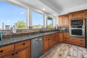 Kitchen featuring wood finish cabinetry, stainless steel appliances, decorative backsplash, a textured ceiling, and dark stone counters