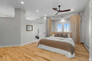 Master bedroom with light wood flooring, baseboard heating, a ceiling fan, and recessed lighting