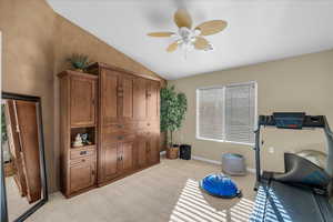 Exercise room with a ceiling fan, vaulted ceiling, and light carpet