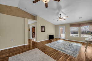 Living room featuring a ceiling fan, vaulted ceiling, and dark wood-type flooring