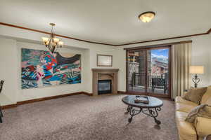 Carpeted living area featuring crown molding, suspended lighting, and a glass covered fireplace