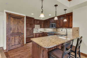 Kitchen with a peninsula, a breakfast bar area, dark wood-style flooring, pendant lighting, and light stone countertops