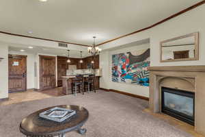 Living room with crown molding, light carpet, suspended lighting, light tile patterned flooring, and a fireplace with flush hearth
