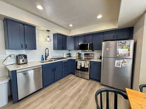 Kitchen featuring stainless steel appliances, blue cabinetry, backsplash, and light wood finished floors