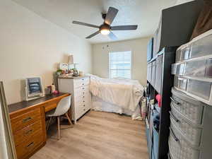 Bedroom featuring an office area, light wood-style flooring, a textured ceiling, and ceiling fan