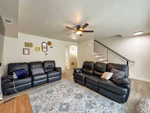 Living room featuring a ceiling fan, a textured ceiling, and light wood finished floors