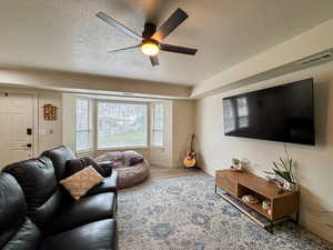 Living area with a textured ceiling, wood finished floors, and ceiling fan