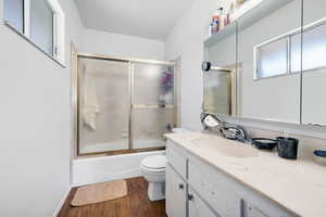 Bathroom with vanity, shower / bath combination with glass door, and dark wood-type flooring