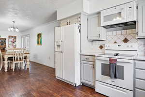 Kitchen featuring white appliances, dark wood-type flooring, suspended lighting, a textured ceiling, and backsplash