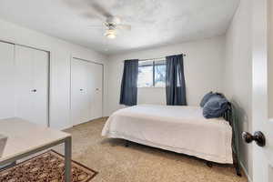Bedroom with two closets, carpet floors, ceiling fan, and a textured ceiling