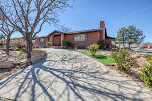 Ranch-style house with a chimney, brick siding, and concrete driveway