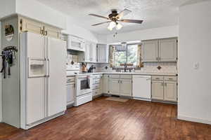 Kitchen featuring white appliances, light countertops, ceiling fan, dark wood-style flooring, and backsplash