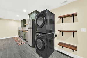Laundry area with stacked washer / drying machine, wood finish floors, and recessed lighting