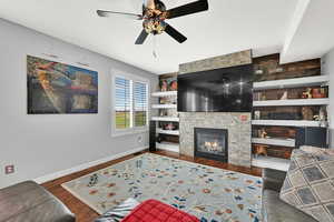 Living room with built in shelves, a fireplace, dark wood-style floors, and a ceiling fan