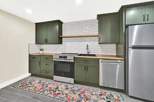 Kitchen with green cabinetry, stainless steel appliances, wooden counters, tasteful backsplash, and recessed lighting
