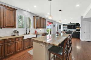 Dual tone kitchen featuring backsplash, light stone counters, dark wood-type flooring, a kitchen bar, and dual tone cabinets