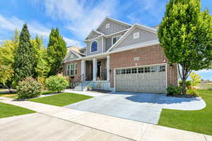 Craftsman-style home featuring board and batten siding, concrete driveway, a front lawn, an attached garage, and covered porch