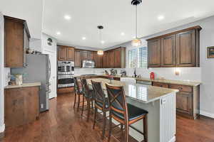 Kitchen featuring a kitchen breakfast bar, light stone counters, a kitchen island, stainless steel appliances, and pendant lighting