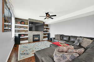 Living area with a fireplace, dark wood-style floors, built in features, and ceiling fan