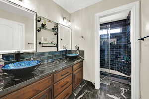 Full bath with double vanity, a stall shower, and dark marble finish floors