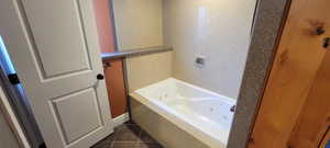 Bathroom with a jetted tub and dark tile patterned flooring