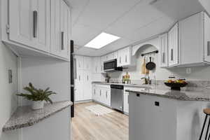 Kitchen featuring a drop ceiling, a peninsula, white cabinets, light stone counters, and light wood-style flooring