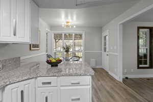 Kitchen featuring white cabinets, a peninsula, light stone countertops, light wood-type flooring, and a chandelier