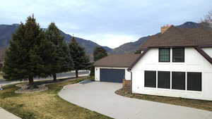 View of side of home featuring a chimney, a mountain view, a garage, concrete driveway, and a yard