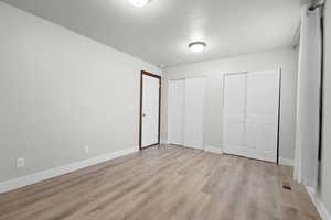 Unfurnished bedroom featuring multiple closets, a textured ceiling, and light wood-type flooring