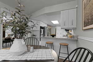 Kitchen featuring a kitchen bar, light wood-style floors, white cabinetry, light stone countertops, and stainless steel appliances