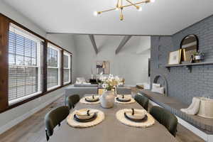 Dining space with brick wall, suspended lighting, wood finished floors, and lofted ceiling with beams