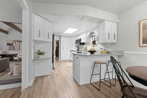 Kitchen with white cabinetry, light stone countertops, light wood-type flooring, a breakfast bar area, and a peninsula