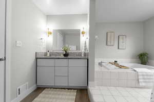 Full bath with double vanity, a garden tub, and light wood-type flooring