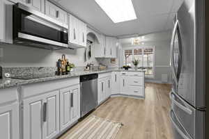 Kitchen with stainless steel appliances, light stone countertops, white cabinetry, light wood finished floors, and a peninsula