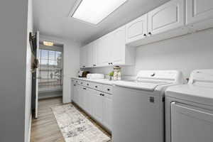 Laundry room featuring separate washer and dryer, light wood finished floors, and cabinet space