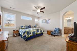 Bedroom with light carpet, ceiling fan, arched walkways, and ensuite bath