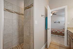 Bathroom featuring connected bathroom, vanity, light wood-type flooring, tiled shower, and a ceiling fan