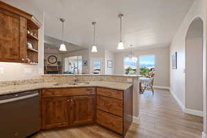 Kitchen with a peninsula, stainless steel dishwasher, light stone counters, and light wood-style floors