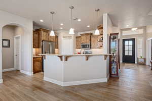 Kitchen with wood finish cabinets, a kitchen breakfast bar, open shelves, decorative light fixtures, and light wood-type flooring