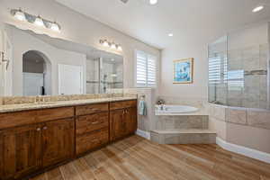Full bath featuring double vanity, a walk in shower, a garden tub, and wood finish floors