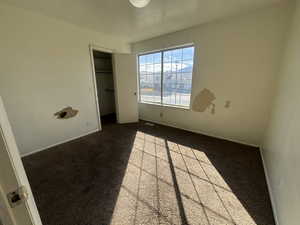 Unfurnished bedroom with a spacious closet and dark colored carpet
